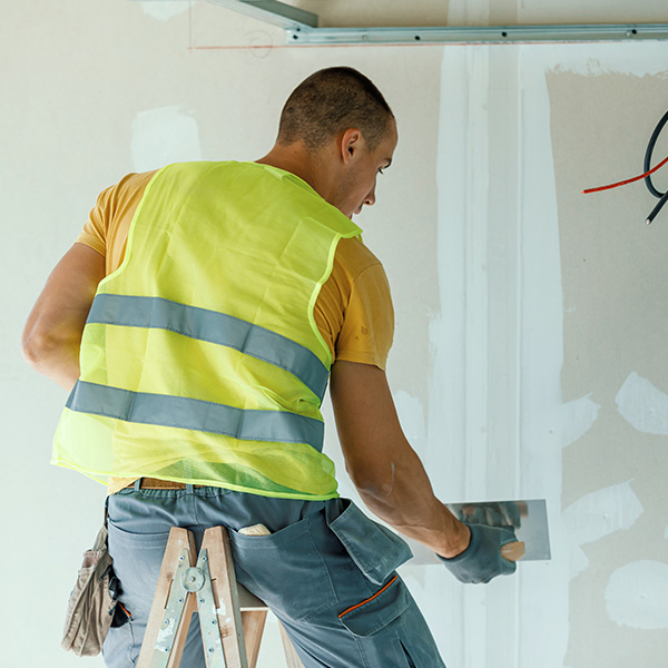 Construction worker sitting on a ladder fixing holes with plaster